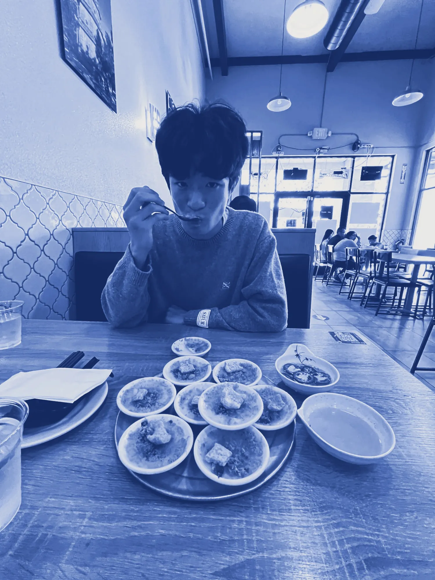 Ian at a restaurant table, mid-bite, with a tray of small dishes in front of him, printed in cyanotype blue.